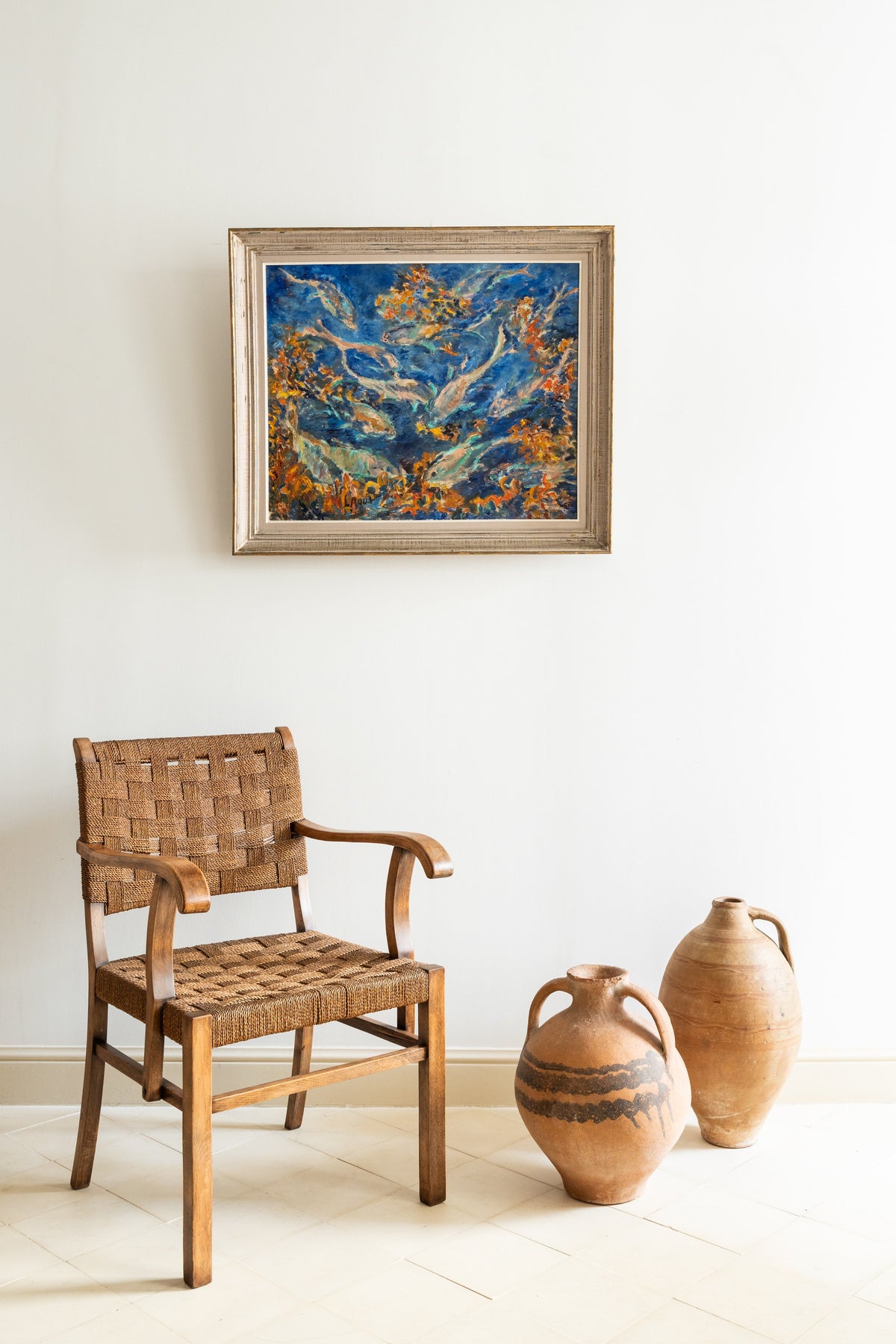 Woven rope armchair and terracotta jars beneath a painting